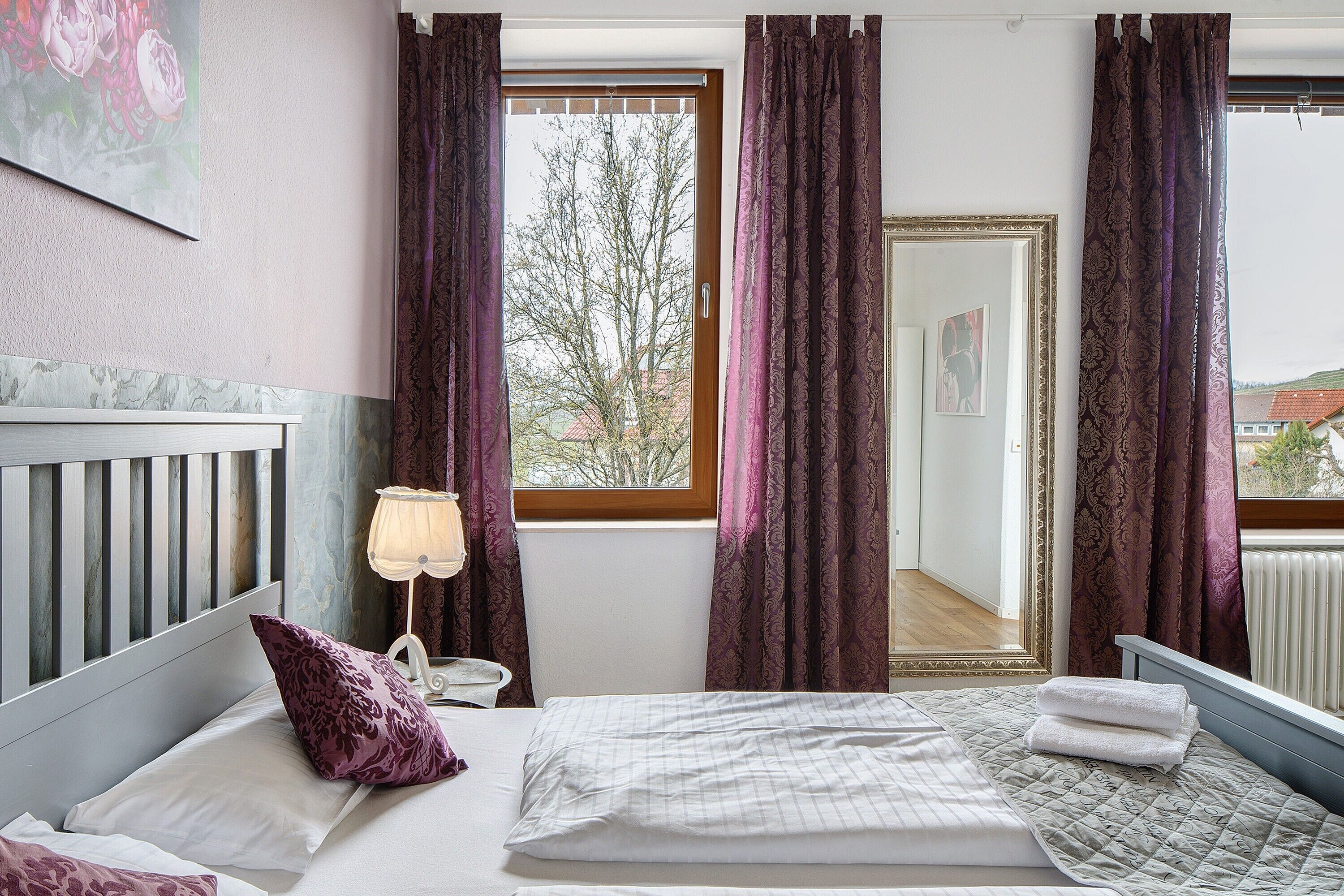 A bedroom with a bed, pillows, a bedside table, a lamp, and a window with curtains.