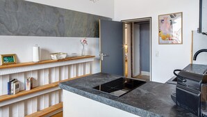 Una cocina moderna con encimera negra, estufa integrada y una puerta que da a otra habitación.