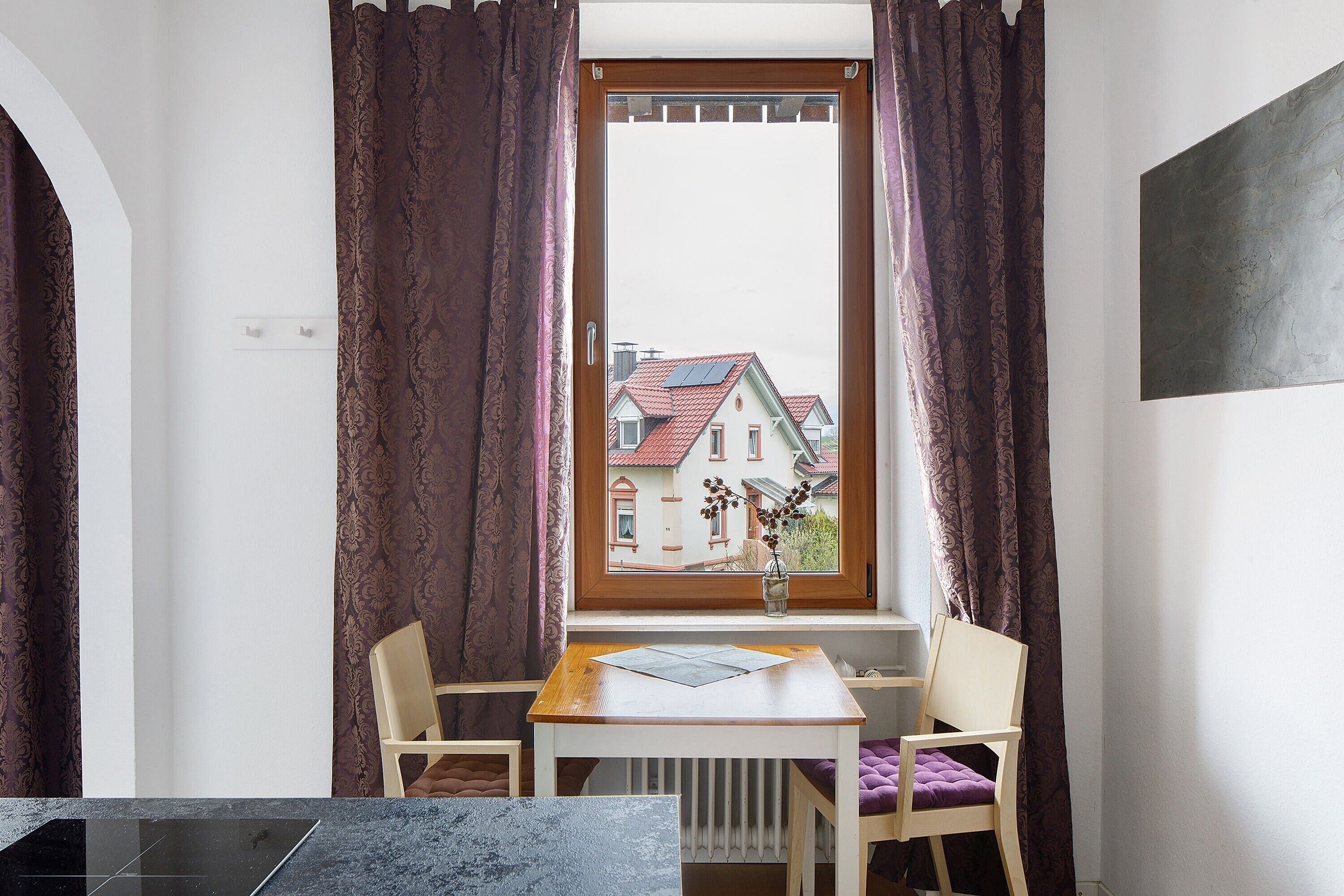 Ein Zimmer mit Fenster, Tisch, zwei Stühlen und Heizkörper.