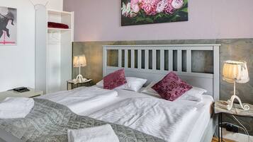 Een tweepersoonsbed met hoofdeinde, twee bedlampen, een nachtkastje, een garderobe en een bloemschilderij aan de muur.