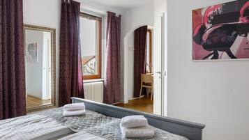 Una habitación de hotel con cama, espejo, ventana con cortinas, una silla y un cuadro en la pared.