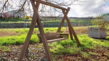 A wooden swing set in a grassy area with a stone structure nearby.