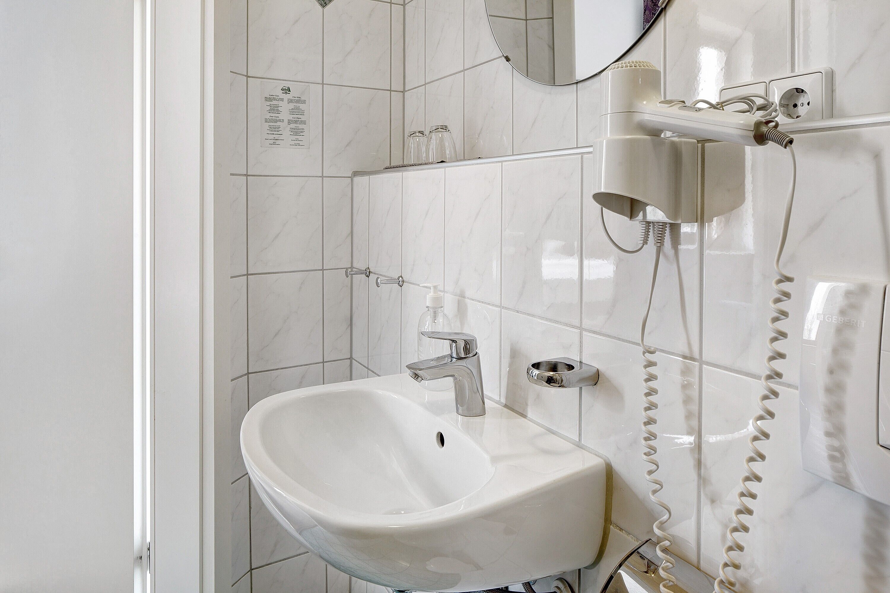 Een badkamer met een witte wastafel, een spiegel en een föhn bevestigd aan de muur.