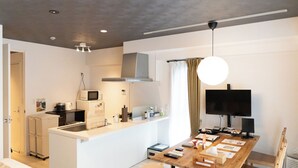 Una cocina compacta con microondas, estufa y lavamanos, un comedor con mesa y sillas de madera, y un televisor montado en la pared.