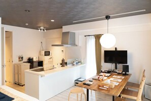 Una cocina compacta con microondas, estufa y lavamanos, un comedor con mesa y sillas de madera, y un televisor montado en la pared.
