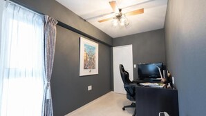Ein Zimmer mit Deckenventilator, Schreibtisch mit Computer, Stuhl und Fernseher.