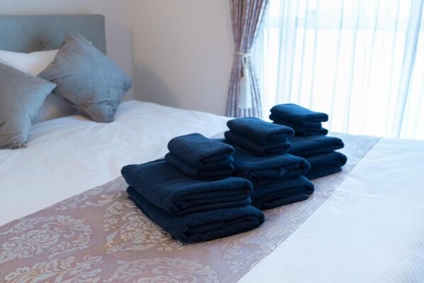 Una cama bien tendida con una pila de toallas dobladas y una colcha estampada.