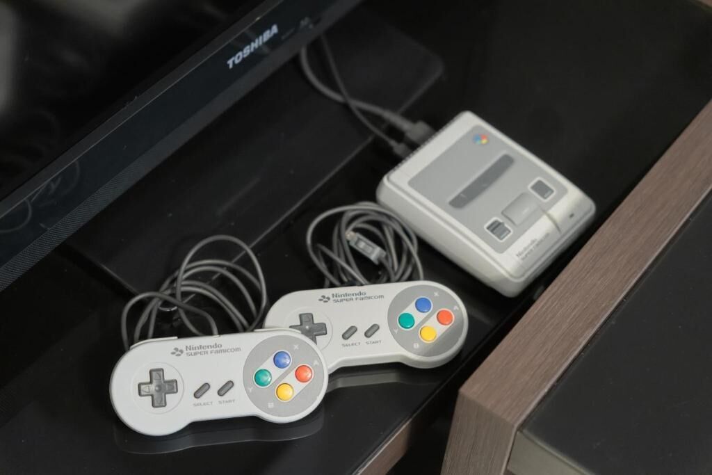 A Nintendo Super Famicom console with two controllers and a cartridge on a black surface.