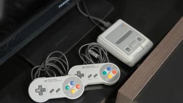 A Nintendo Super Famicom console with two controllers and a cartridge on a black surface.
