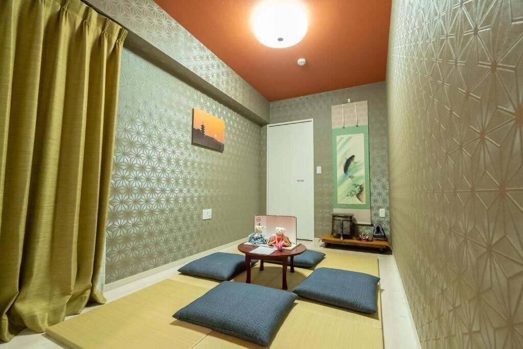 A room with tatami mats, a tatami mat table, cushions, a small shelf with items, and a door.
