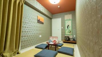 A room with tatami mats, a tatami mat table, cushions, a small shelf with items, and a door.