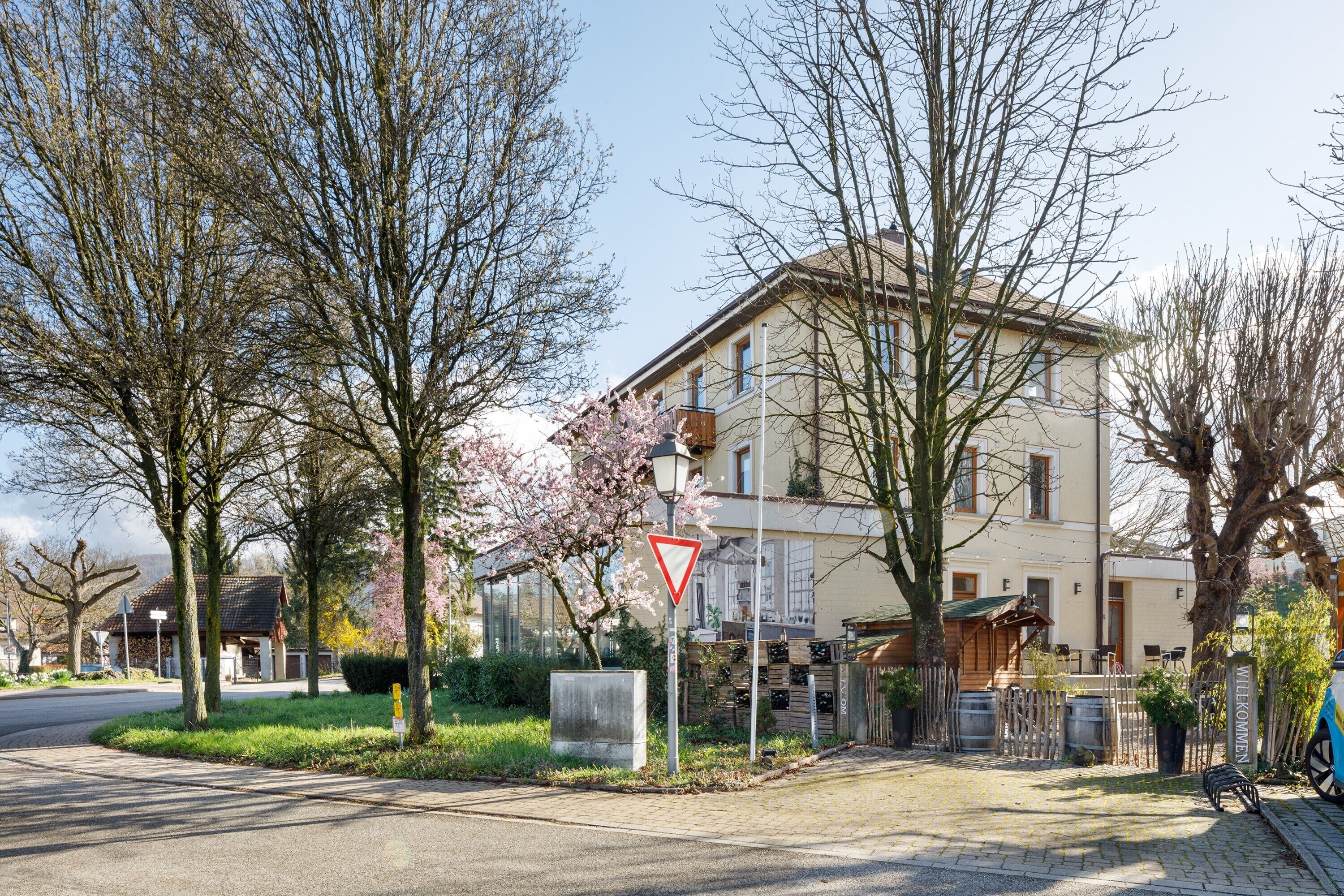 A residential street with a triangular yield sign, a welcome sign, and a building with a balcony.