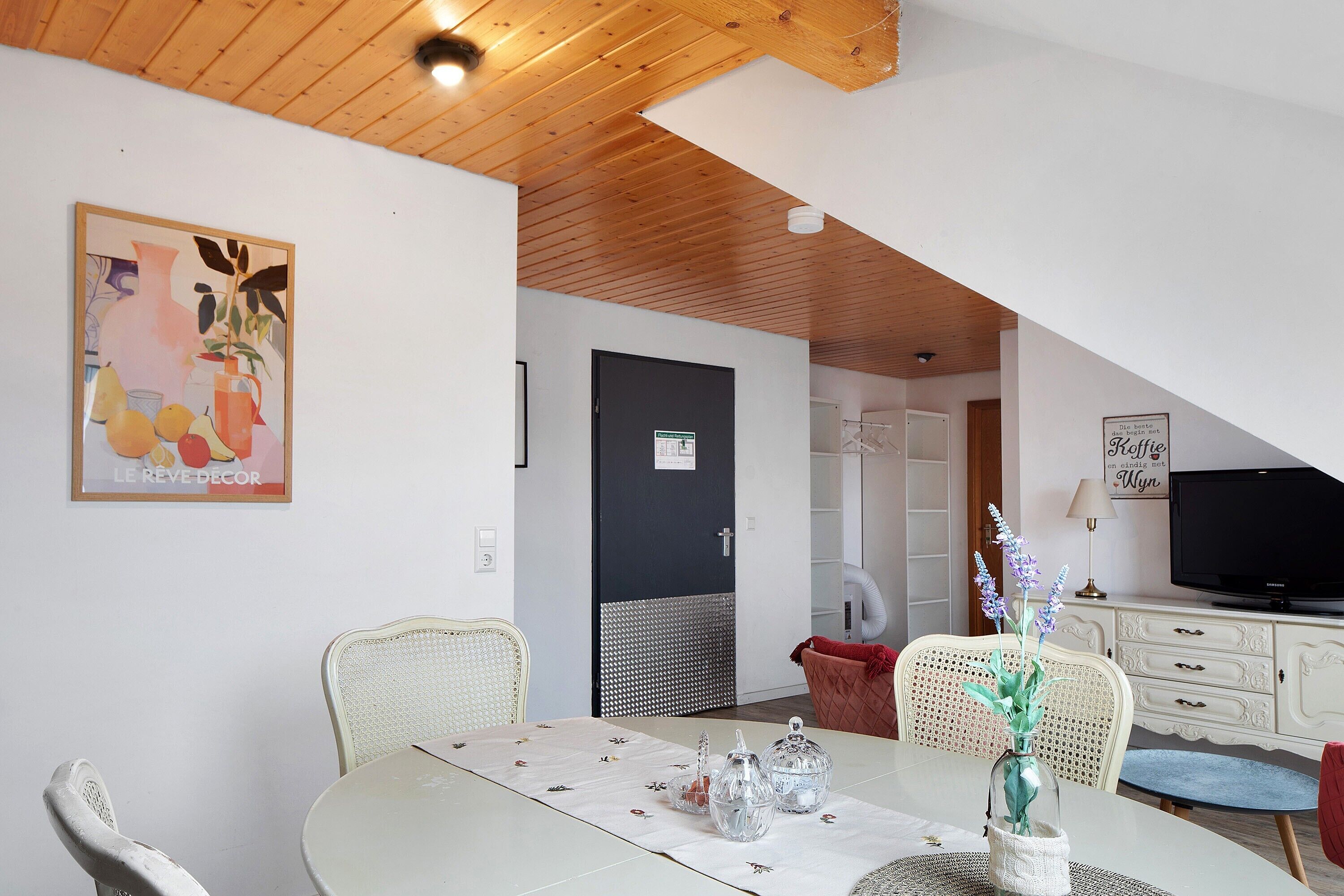 A dining area with a table set for two, a television, and a door leading to another room.