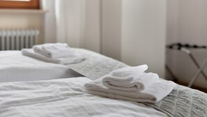 Een netjes opgemaakt bed met gevouwen witte handdoeken, een radiator en een raam met gordijnen.