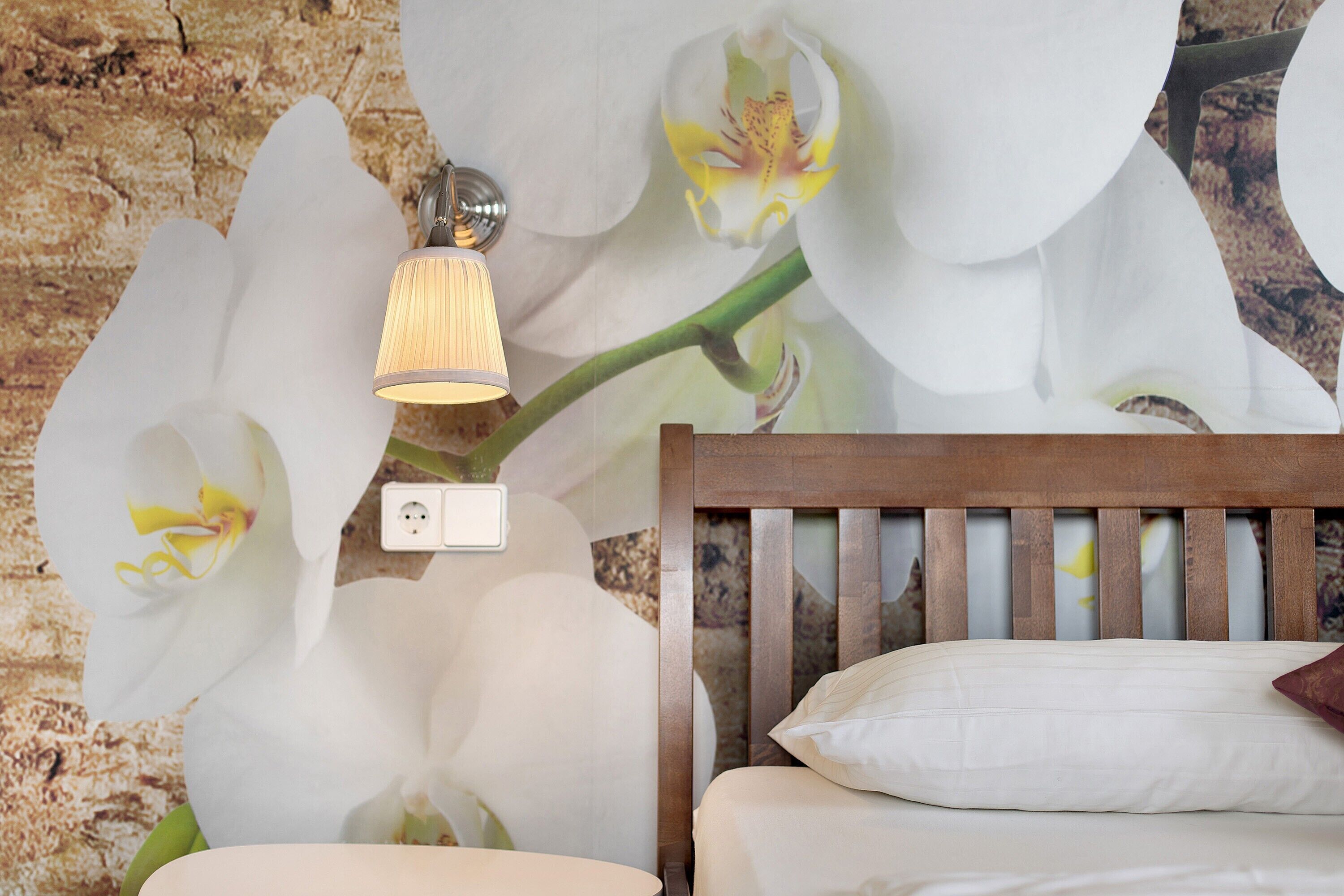 Quarto com cabeceira de madeira, travesseiro branco e luminária fixada na parede.