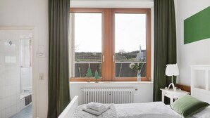 Un dormitorio con cama, mesita de noche, ventana con cortinas, radiador y vistas al exterior.