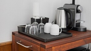 Una bandeja con vasos, tazas y una cafetera sobre una superficie de madera.