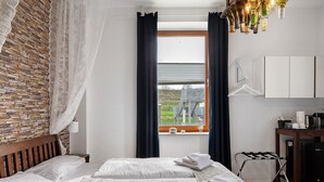 Hotelkamer met een bed, een houten hoofdbord, een raam met gordijnen, een klein tafeltje met een waterkoker en een wandlamp.