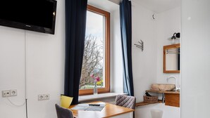 Een kamer met een eettafel, een stoel, een raam met gordijnen, een wastafel en een aan de muur bevestigde televisie.