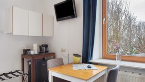 Een compacte kamer met een kitchenette, een eettafel, een aan de muur bevestigde televisie en een raam met uitzicht op bomen.