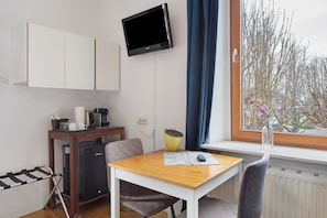 A compact room with a kitchenette, a dining table, a TV mounted on the wall, and a window with a view of trees. - Room "Rebhütte" with Shared Garden and Wi-Fi (Vogtsburg im Kaiserstuhl)