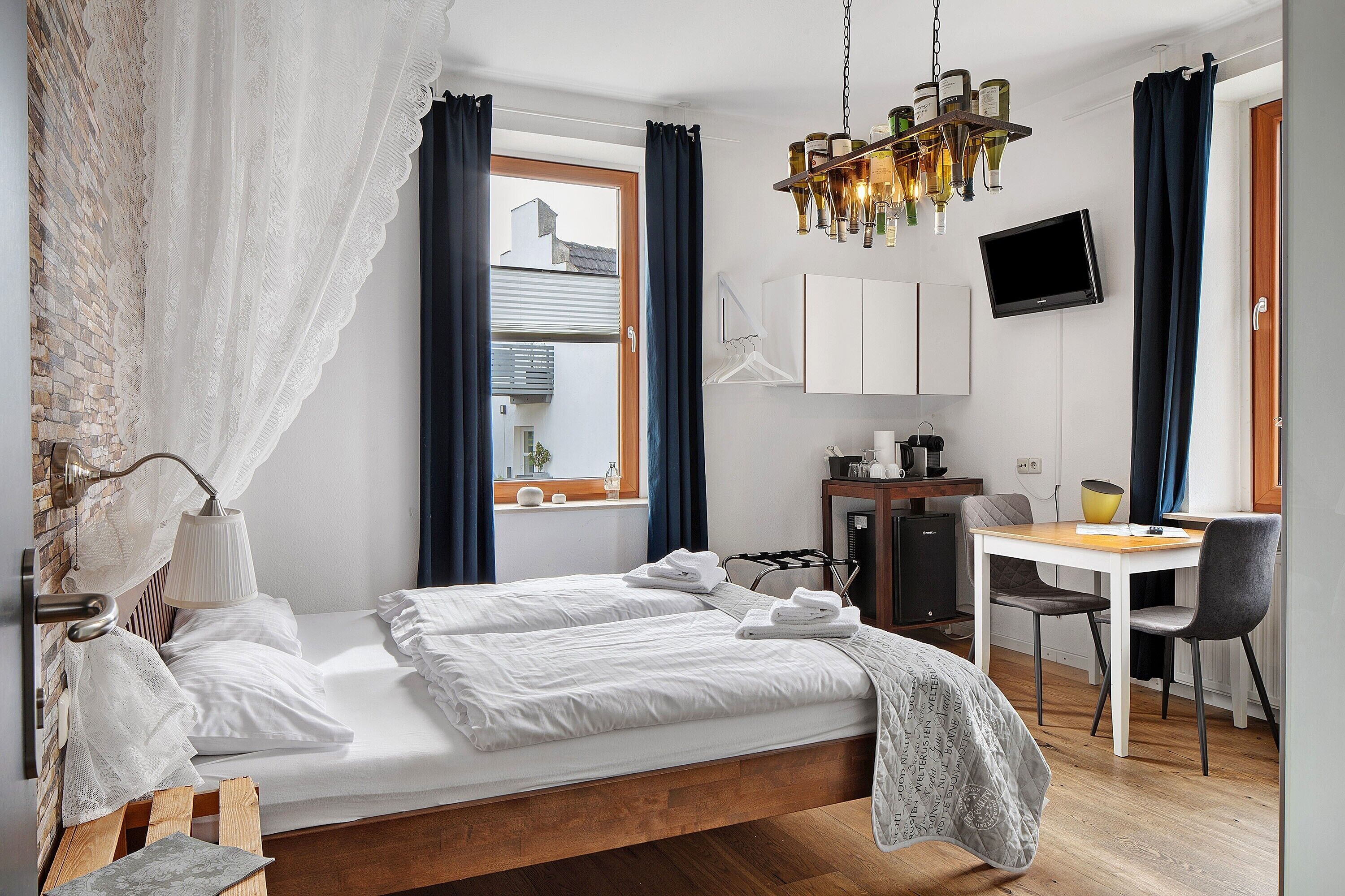 A bedroom with a bed, a desk, a chair, a television, and a window with curtains.