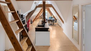 Habitación en ático con escalera de madera, espacio de cocina con estufa y mesa de comedor con sillas.