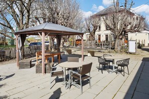 En uteplats med en pergola, utomhusmöbler och utsikt över ett hus och träd.
