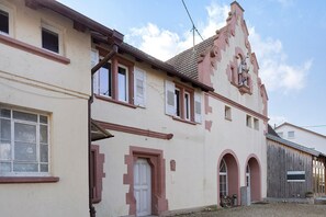 Un bâtiment de style architectural traditionnel, caractérisé par une entrée arquée imposante, de nombreuses fenêtres avec volets et une cheminée bien visible.