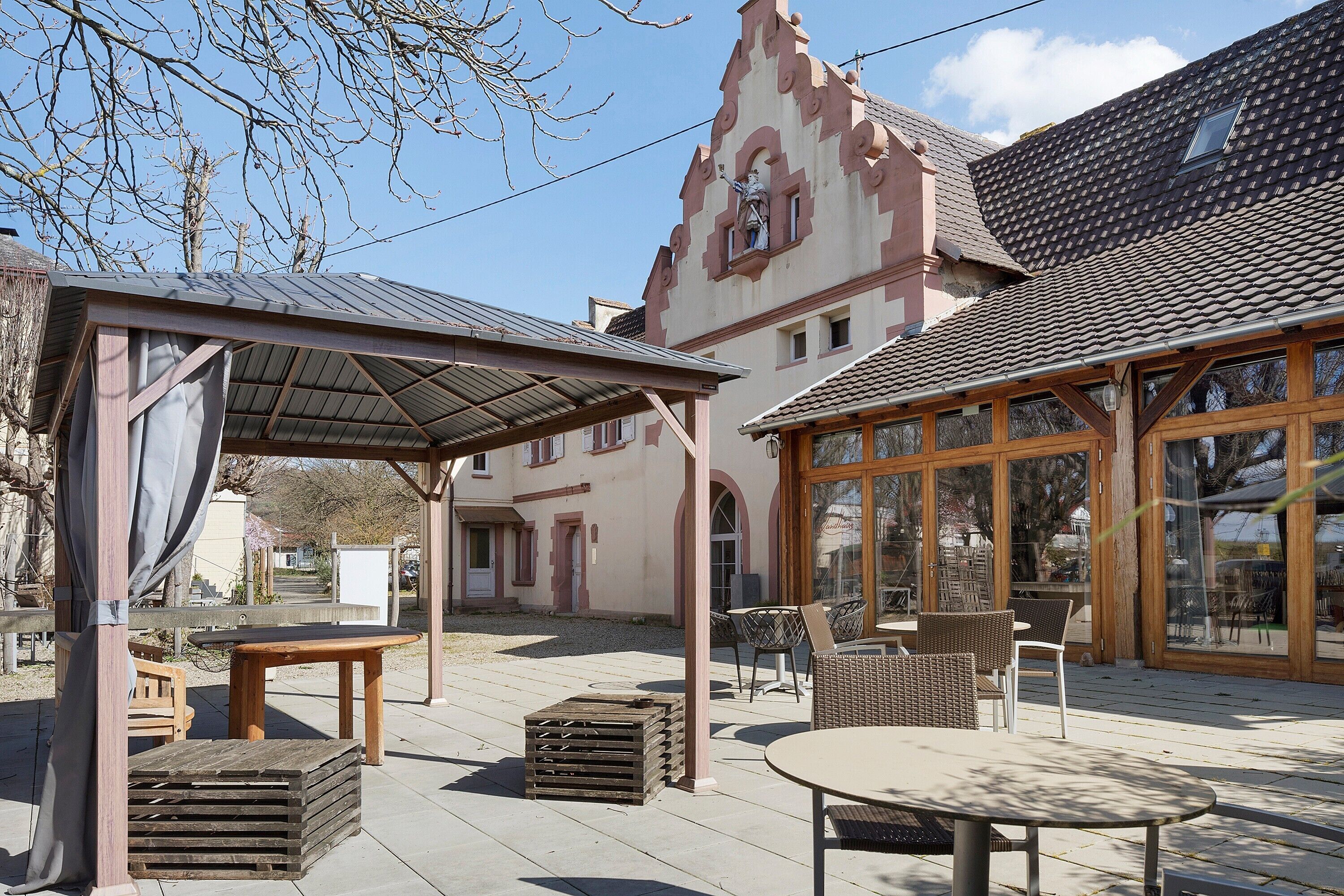 Ein Innenhof mit Sitzgelegenheiten im Freien, einer Pergola und einem Gebäude mit markanter Architektur.