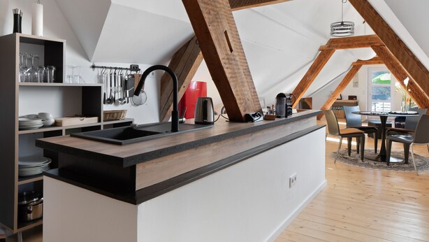 Una cocina moderna con una isla central, vigas de madera y un comedor con sillas y una mesa.