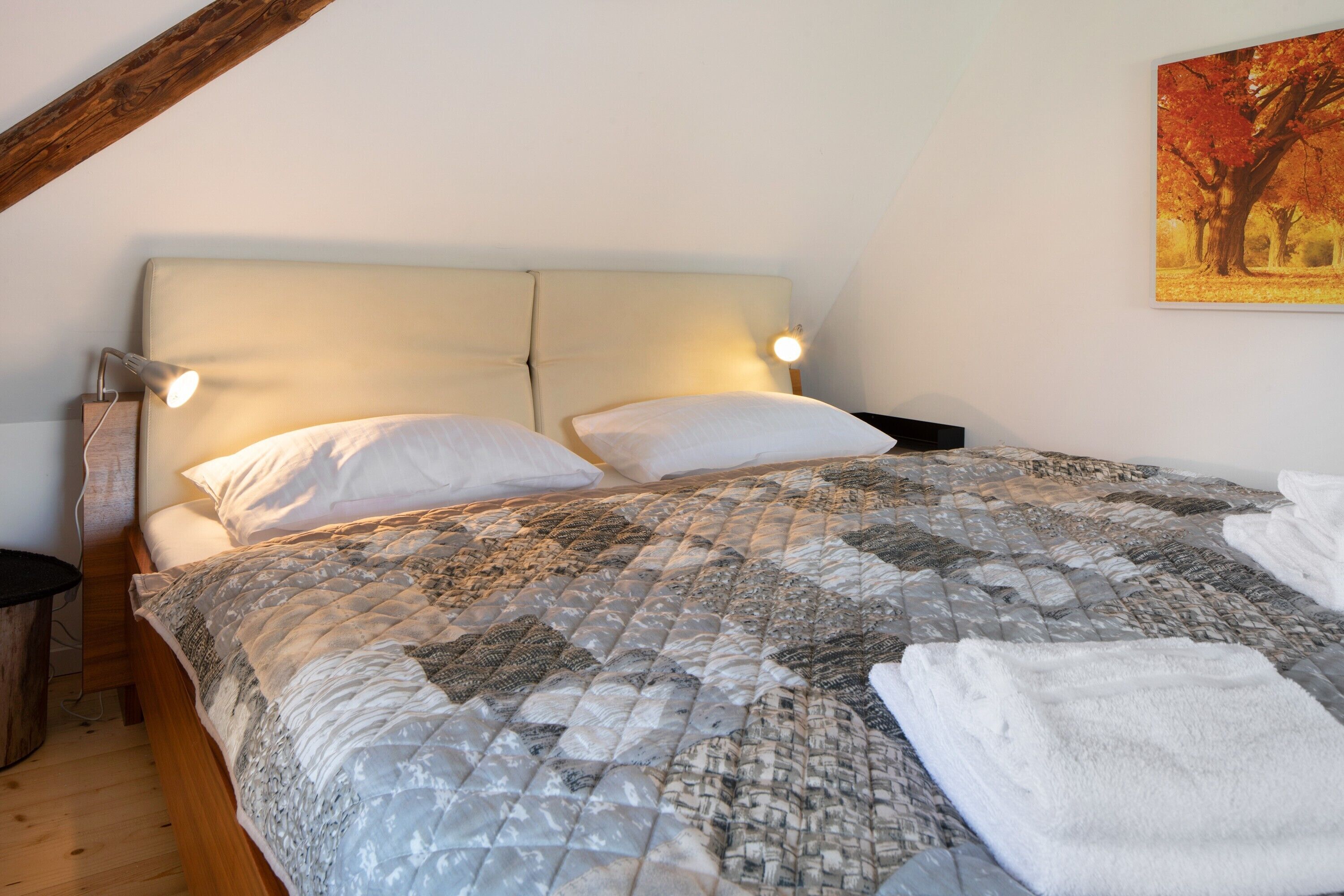 Ein Schlafzimmer mit einem Bett, zwei Nachttischlampen, Holzboden und einem Bild an der Wand.