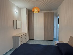 A bedroom with a bed, a dresser, a mirror, a wardrobe, and a hanging light fixture.