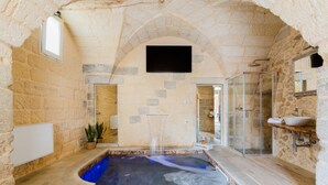 A stone-walled spa area with a hot tub, a shower, and a sink.