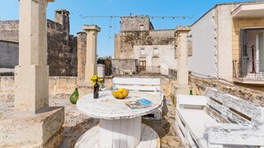 A rooftop terrace with a round table, a bowl of lemons, a bottle of wine, and a magazine.