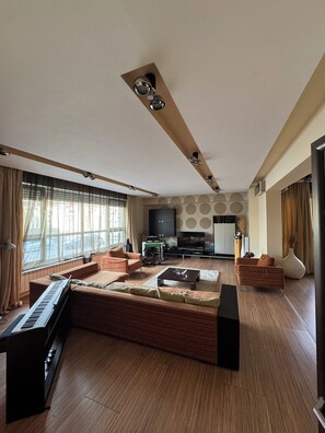 Een moderne woonkamer met een hoekbank, een piano, een televisie en een groot raam met gordijnen.