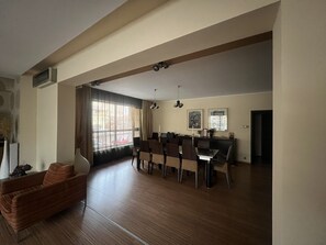 Ein großzügiger Wohnbereich mit Esstisch und Stühlen, einer Couch und einem großen Fenster mit Vorhängen.