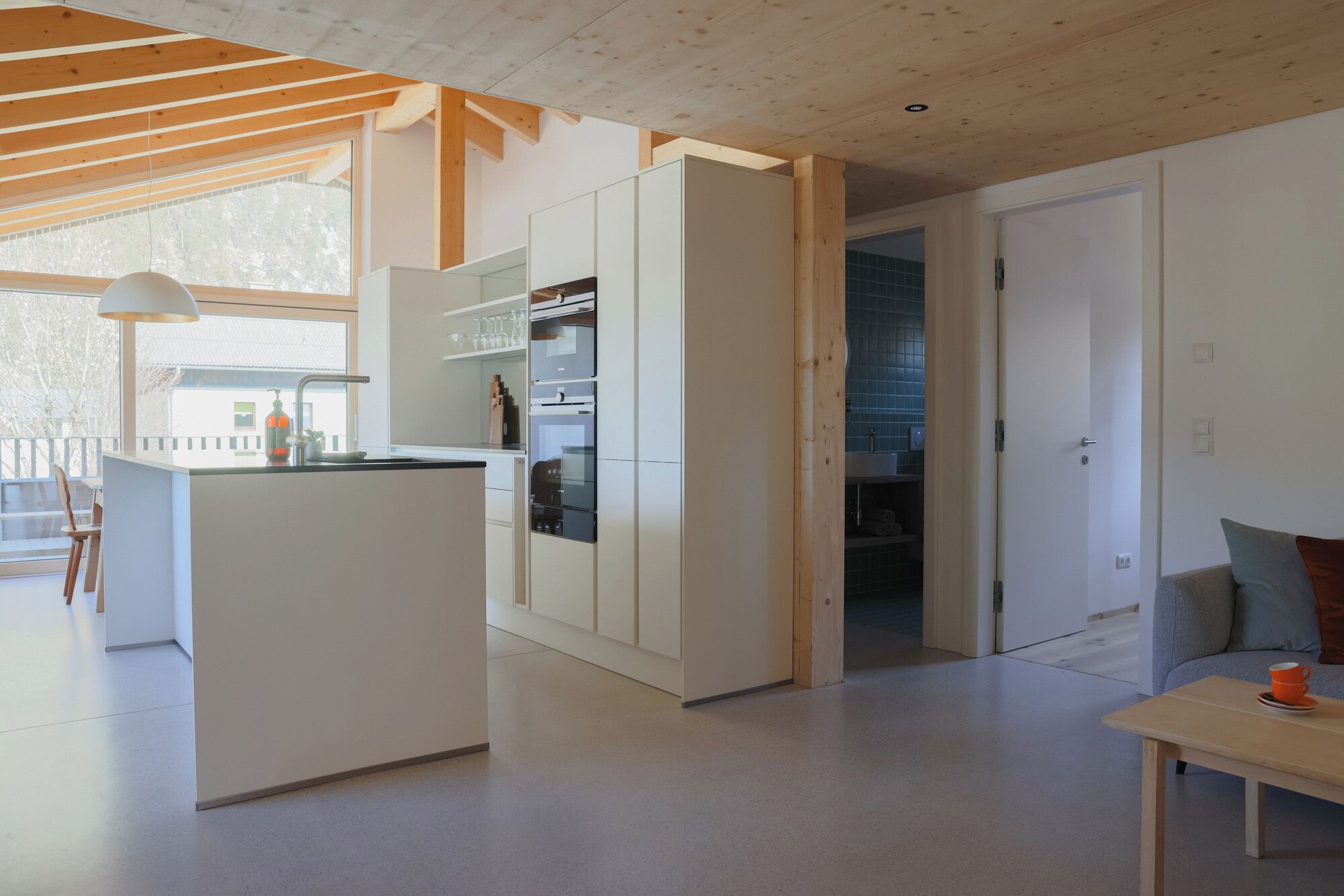 A modern kitchen with white cabinetry, a dining area with a table and chairs, and a view of the outdoors through large windows.