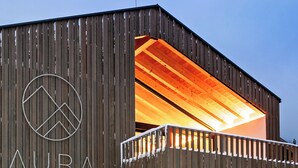 Un edifici amb façana de fusta, un logotip circular i el text 'AURA KARWENDEL' al costat.
