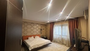 Una habitación de hotel con cama, televisión, escritorio y ventana con cortinas.