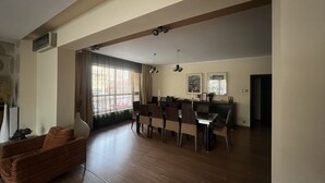 Un salón amplio con una mesa de comedor y sillas, un sofá, y un ventanal con cortinas.