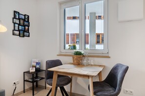 Un espace repas comprenant une table, des chaises, une petite table d’appoint avec un panneau indiquant la présence d’une connexion Wi-Fi, et une fenêtre donnant sur des bâtiments.