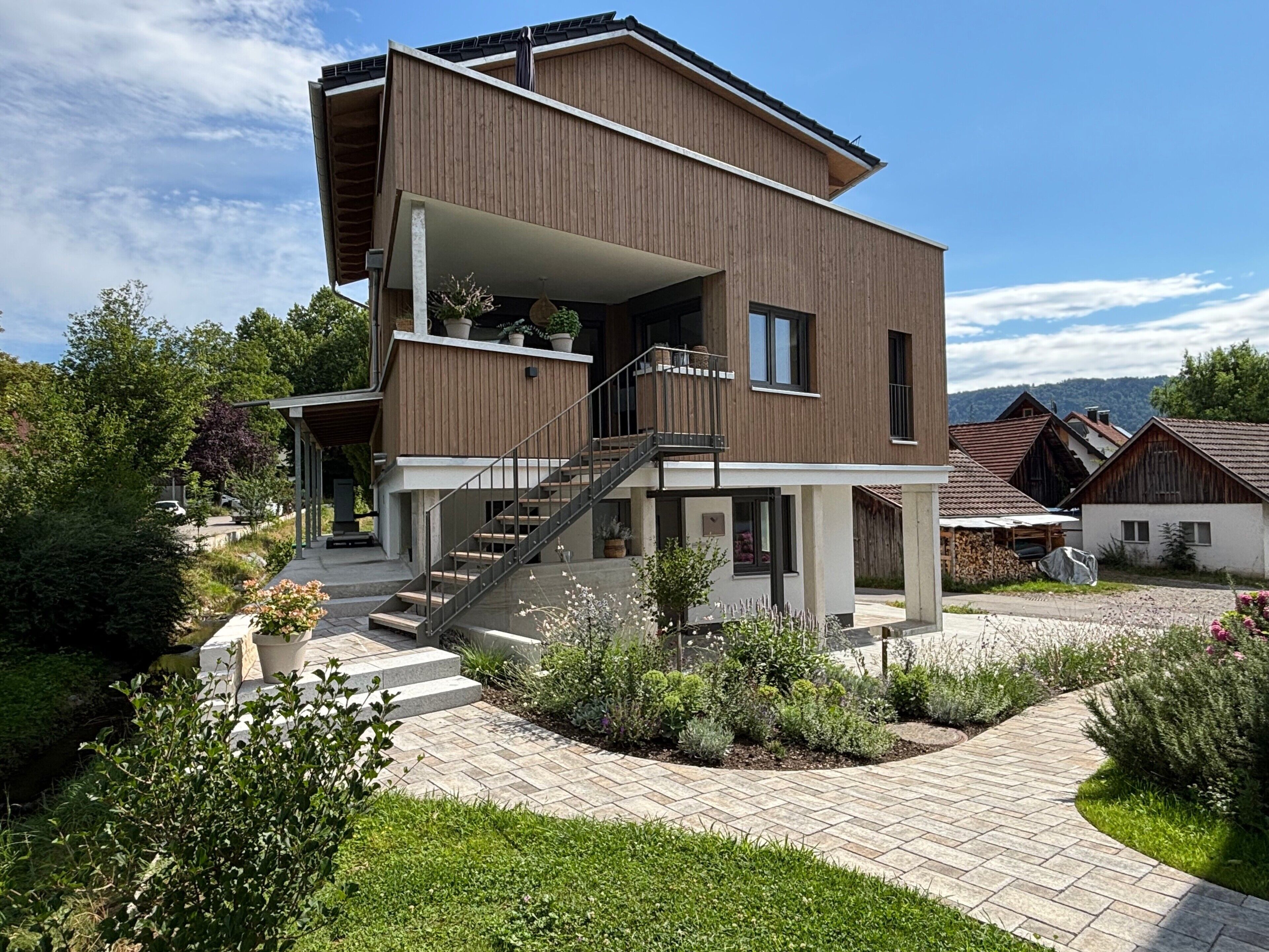 Une maison moderne à deux étages, dotée d’un balcon, d’un escalier et d’un jardin.