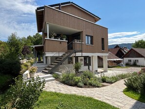 Une maison moderne à deux étages, dotée d’un balcon, d’un escalier et d’un jardin.