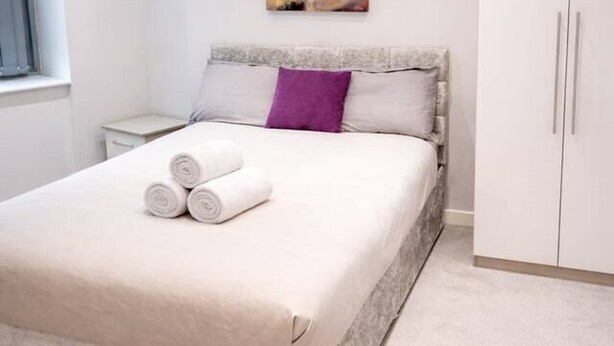Un dormitorio moderno con una cama grande, una mesita de noche, un armario y un cuadro en la pared.