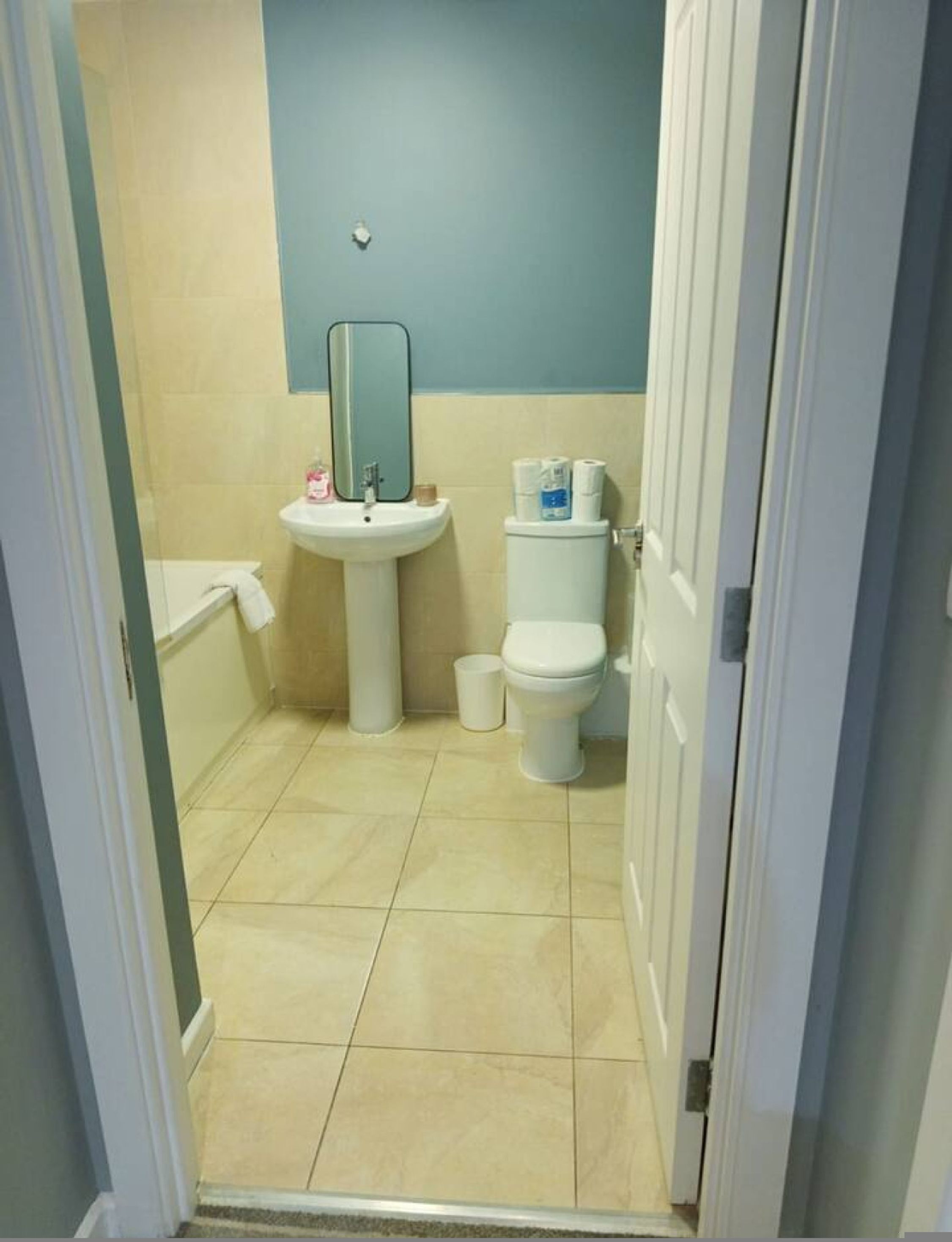A small bathroom with a sink, mirror, toilet, and a trash bin.