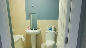 Une petite salle de bain avec un lavabo, un miroir, des toilettes et une poubelle.