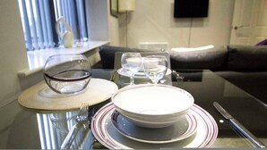 Una mesa de comedor con platos, vasos y cubiertos, un sofá, un televisor y una ventana con cortinas.