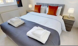 A neatly made bed with white linens, two nightstands with lamps, and a window with blinds. - Cole Green Lane Executive Stay- Free Parking (Welwyn Garden City)