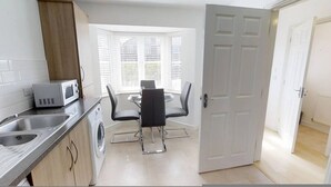 A compact kitchen with a microwave, washing machine, and a dining area with a table and chairs. - Cole Green Lane Executive Stay- Free Parking (Welwyn Garden City)